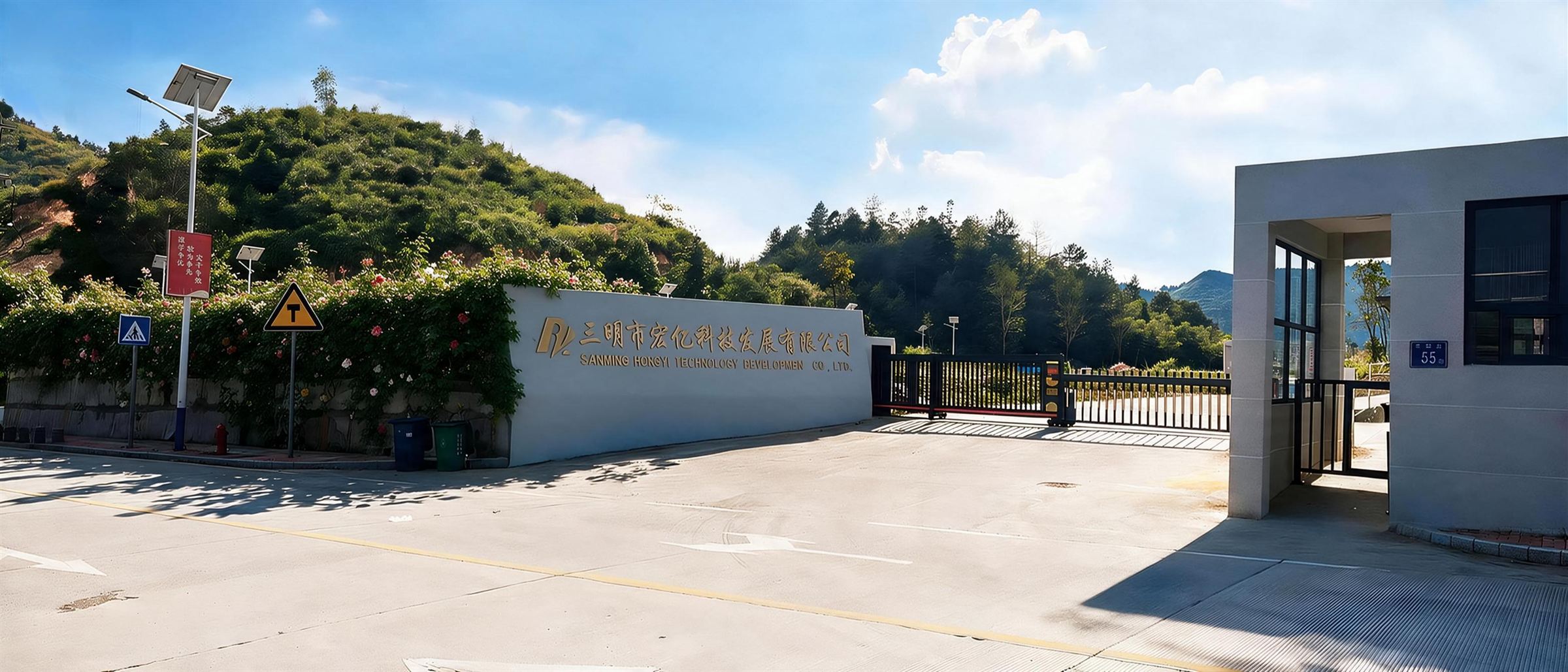 厂区主入口实拍，厂牌墙上是企业中英文全称，右侧为门岗与电动伸缩门